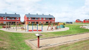 A playground with swings and climbing structures, surrounded by a grassy area and a building with a red facade. - 5 Person Holiday Home on a Holiday Park in Lemvig (Lemvig)