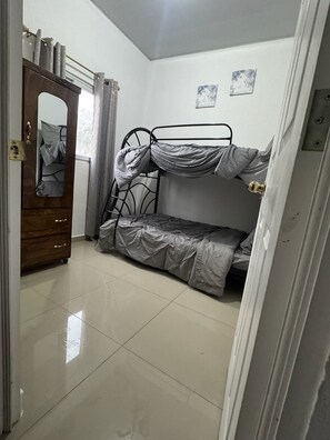 A room with a bunk bed, a wooden wardrobe, and a door with a mirror.