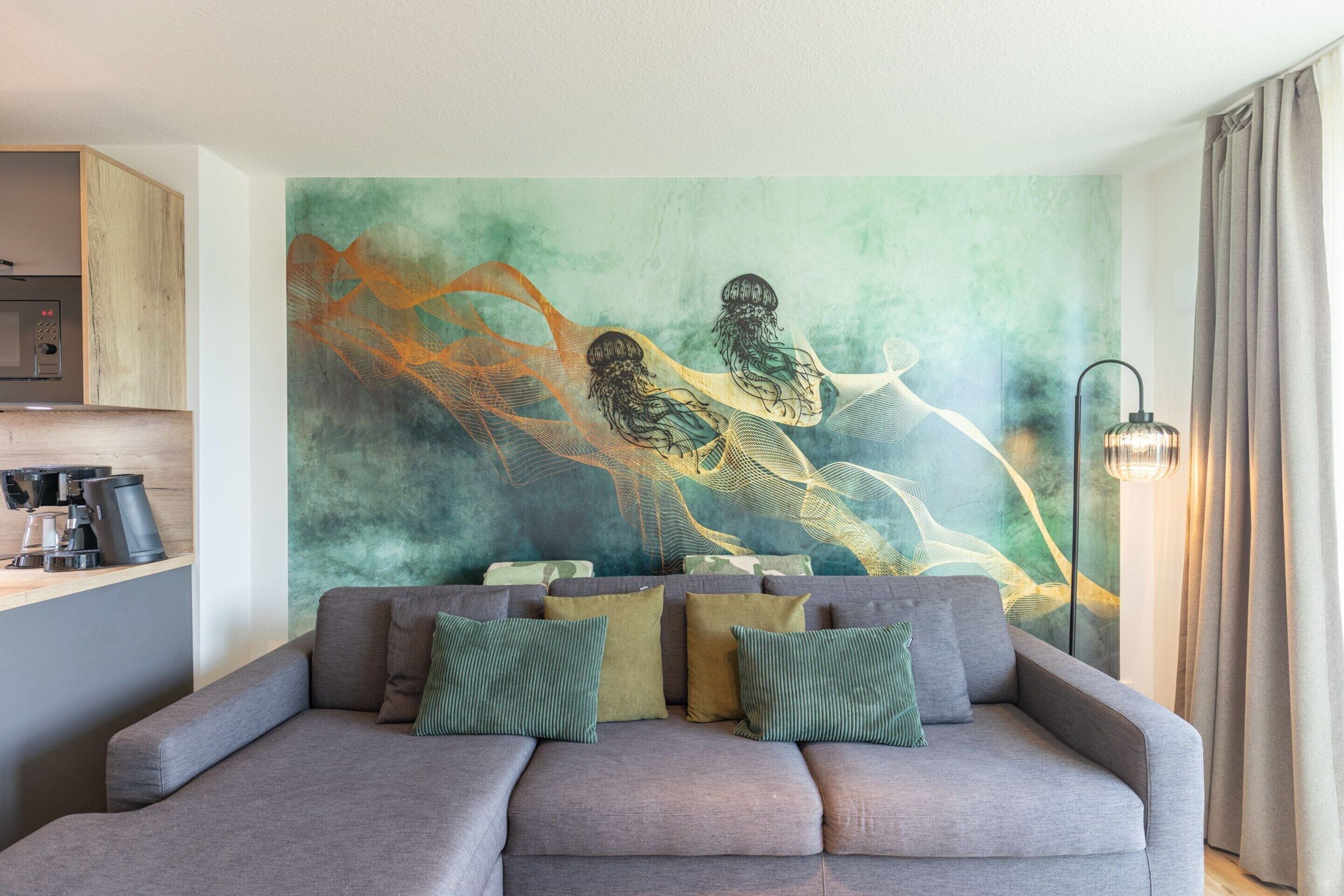 A modern living room with a grey sofa, green and brown cushions, a large abstract painting on the wall, and a coffee machine on the left.