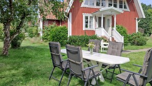 A dining area with a table and four chairs, a house with a red exterior and white trim, and a well-maintained garden. - Awesome home in Söderåkra with WiFi (Söderåkra)