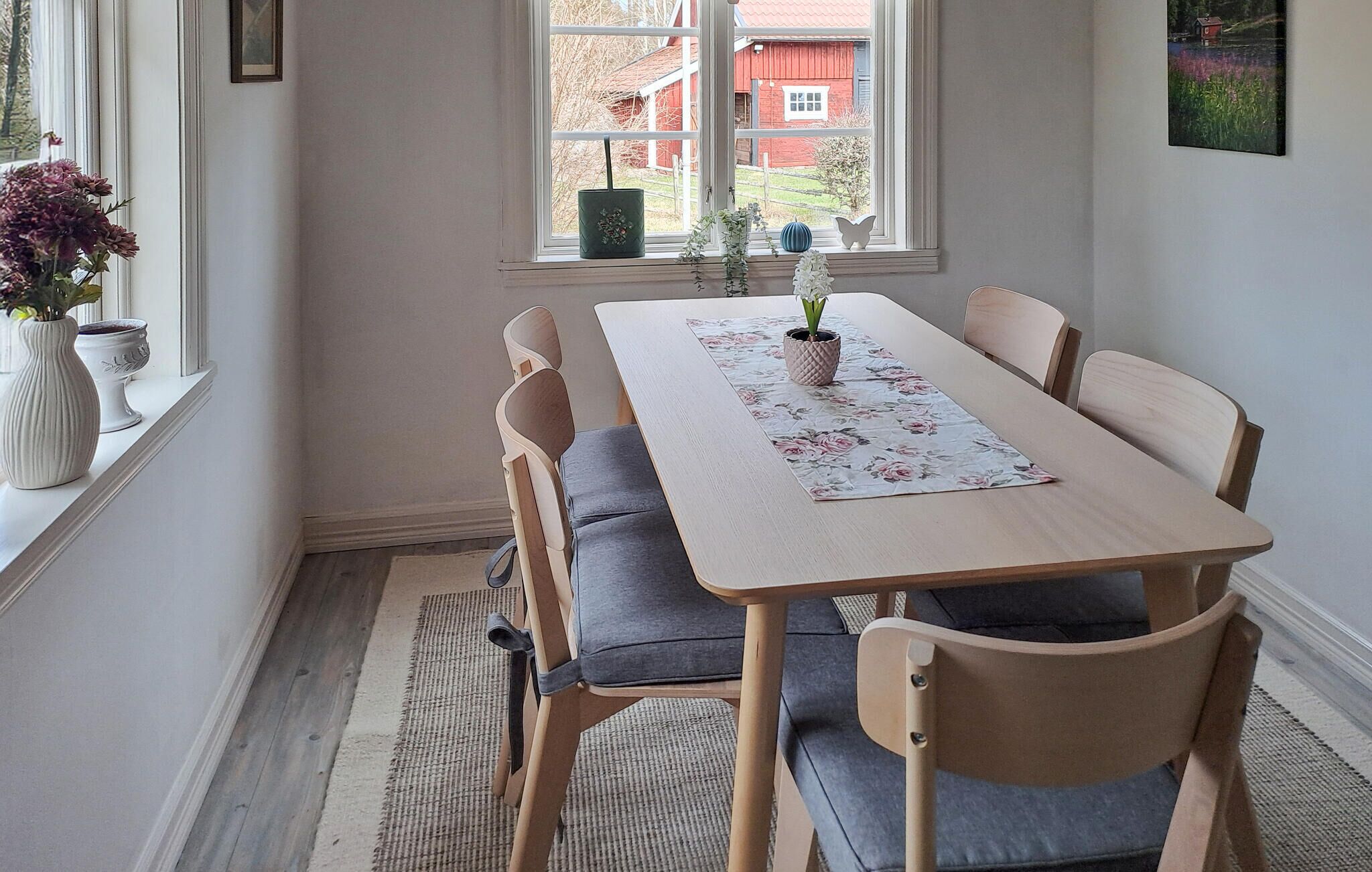 A dining area with a wooden table, grey upholstered chairs, and a floral table runner.