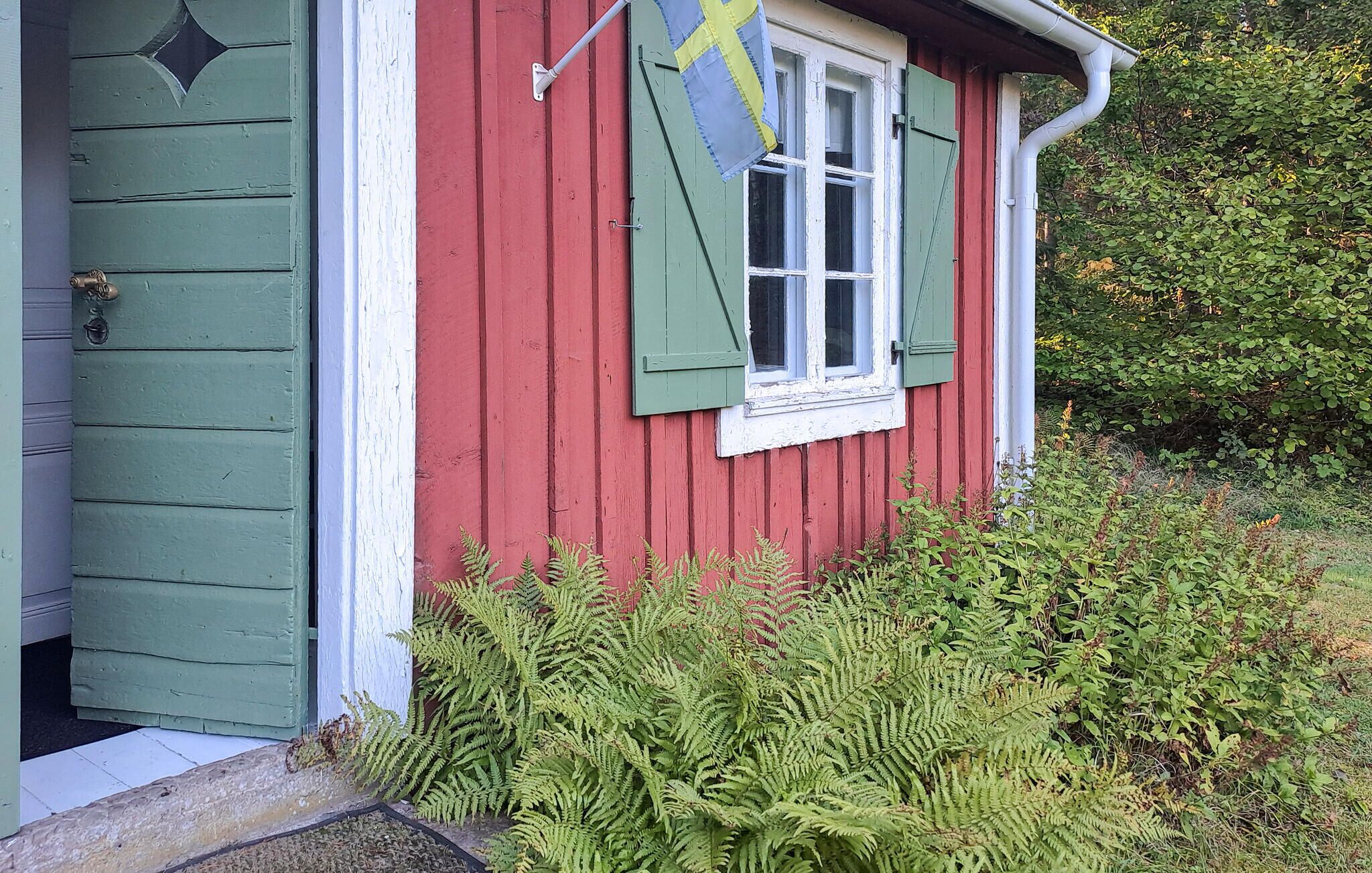 Ein rotes Holzhaus mit einem weißen Fenster und grünen Fensterläden.