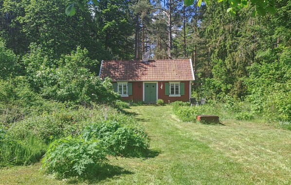 A small, single-story house with a red-tiled roof, surrounded by dense greenery and trees. - Amazing home in Halltorp with WiFi (Halltorp)