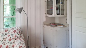 A room with a floral-patterned sofa, a floor lamp, a white cabinet with glass doors, and a window with a green shutter. - Amazing home in Halltorp with WiFi (Halltorp)