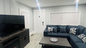 A modern living room with a flat-screen TV, dark wood entertainment unit, a sectional sofa with patterned cushions, and a patterned rug. - Modern cozy apartment (Nutley)