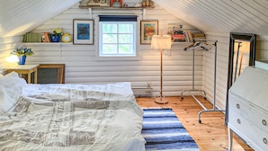 A cozy attic bedroom with a bed, a dresser, a window, and a lamp.