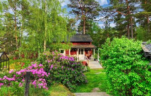 Uma pequena cabana de madeira rodeada por vegetação exuberante e arbustos floridos.