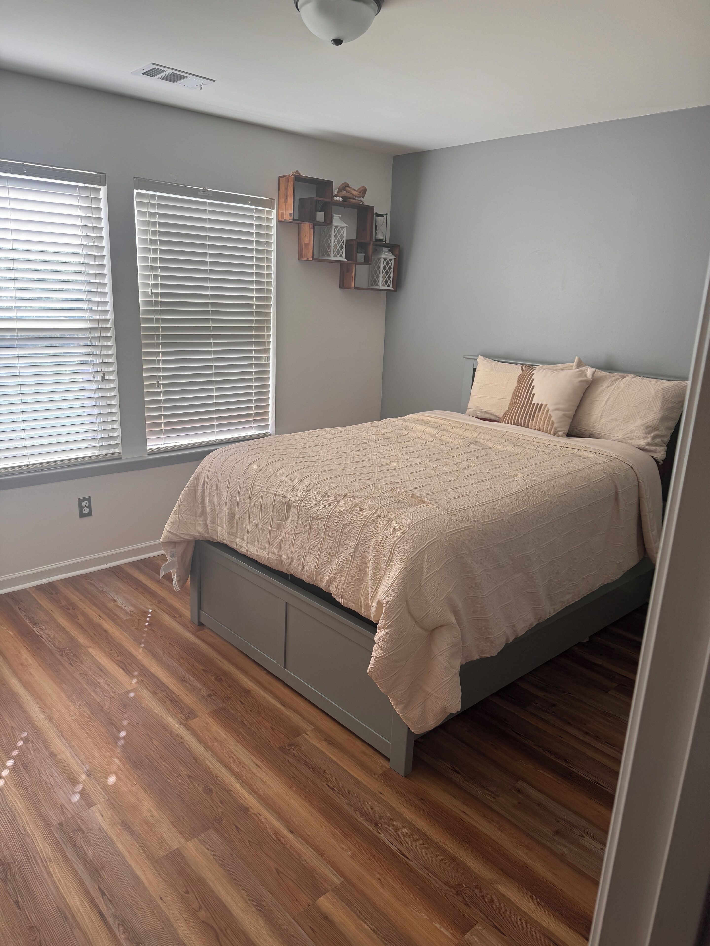 A bedroom with a bed, wooden flooring, a window with blinds, and a ceiling fan.