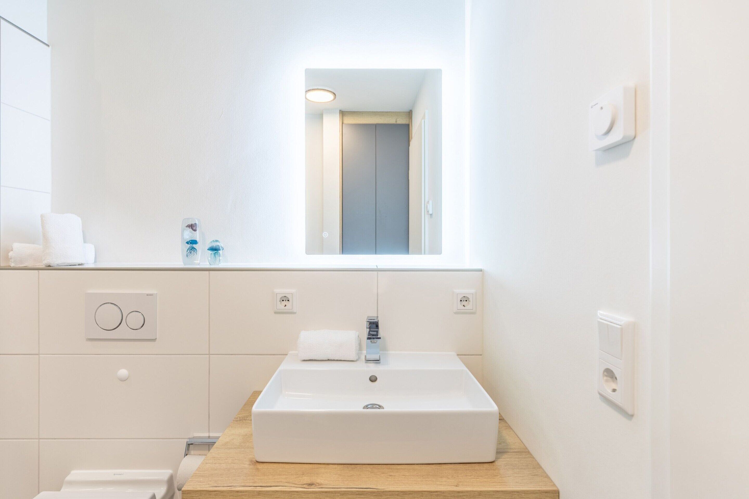 Een moderne badkamer met een rechthoekig wastafelmeubel, een spiegel en een houten blad.