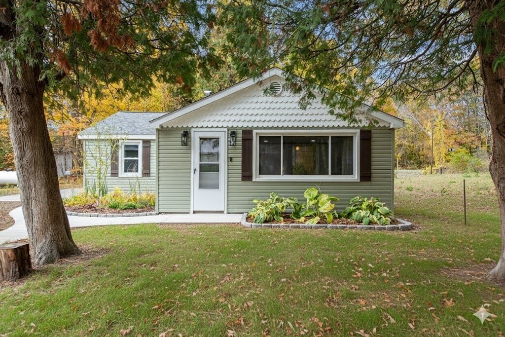 A small, single-story house with a gabled roof, a front porch, and a small garden area with various plants.