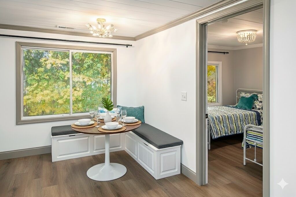 Une chambre d’angle avec une table à manger dressée pour deux personnes, un banc et un lit recouvert d’une courtepointe à rayures.
