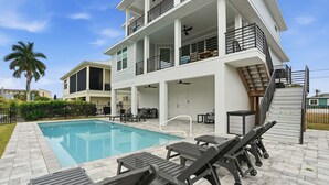 Casa de dos pisos con piscina, mobiliario exterior y una escalera que conduce al piso superior.