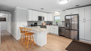 Una cocina moderna con armarios blancos, un refrigerador de acero inoxidable, taburetes de bar de madera y una isla de encimera de mármol.