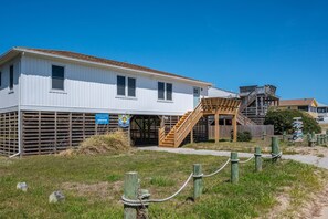 Un bâtiment situé sur la côte, doté d’un escalier en bois menant à une zone abritée, le tout entouré d’une pelouse délimitée par une clôture.