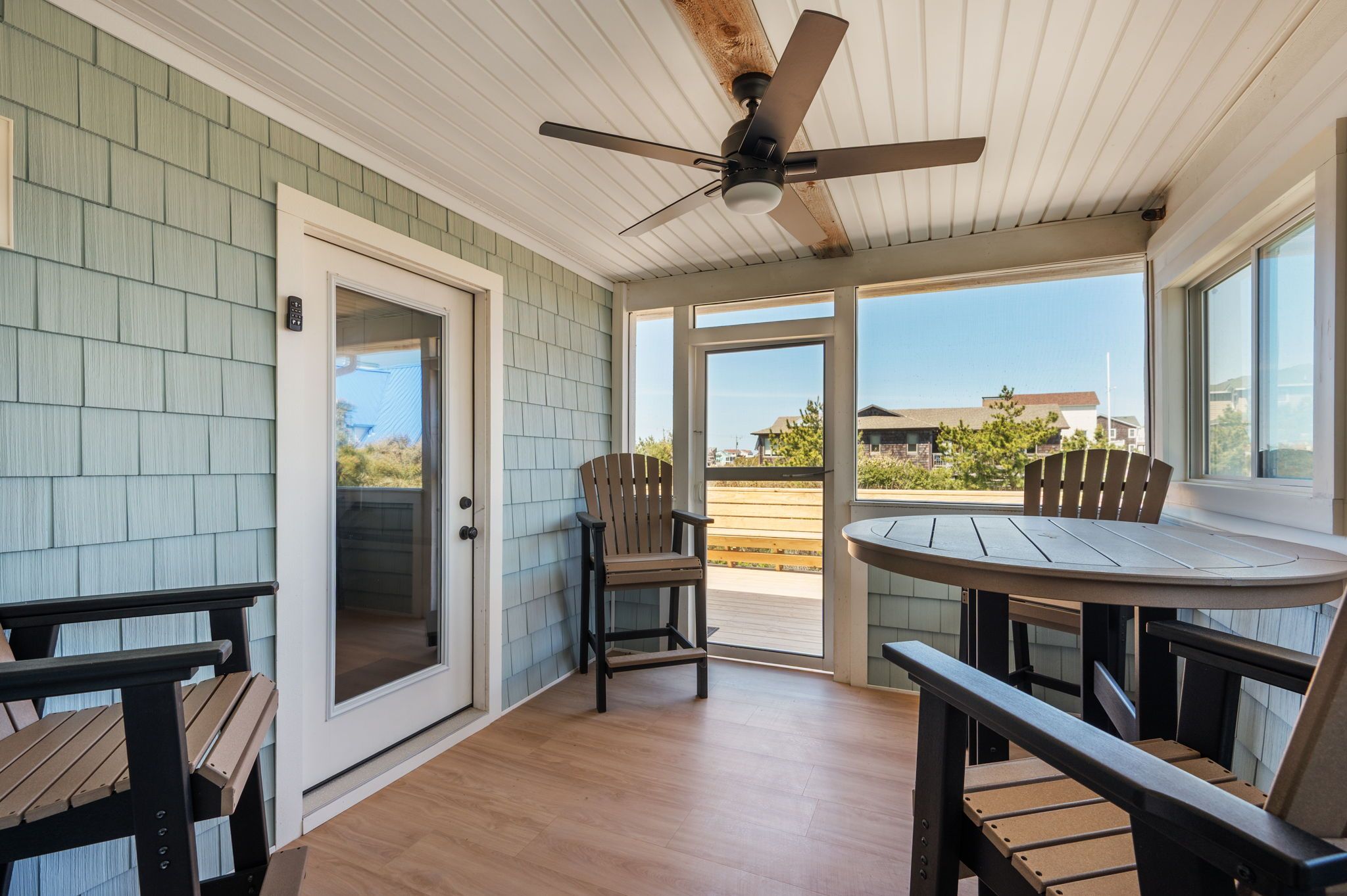 A covered patio area with a ceiling fan, a round table, and two Adirondack chairs.