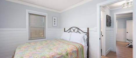 Un dormitorio con cama, una ventana con persianas, una puerta que da a otra habitación y una lámpara en el techo.