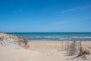Una platja sorrenca amb una tanca de fusta i vegetació dispersa.