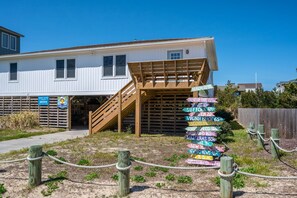 A coastal building with a wooden deck and a signpost with directional arrows. - Luke Anna: Semi-Oceanfront, Close to Beach (Nags Head)