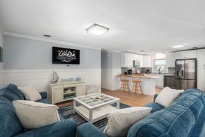 A modern living room with a sofa, coffee table, and a TV mounted on the wall. - Luke Anna: Semi-Oceanfront, Close to Beach (Nags Head)