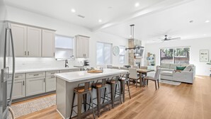 A modern kitchen with a large island, bar stools, and a dining area with a sofa and chairs.