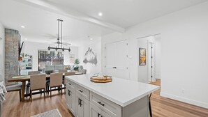 A modern kitchen with a central island, dining area, and a stone accent wall.