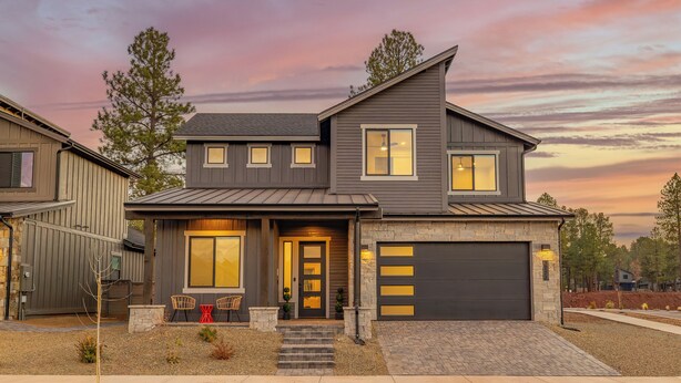A modern two-story house with a garage, a front porch with chairs, and a driveway.