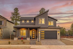 A modern two-story house with a garage, a front porch with chairs, and a driveway. - Modern Escape with Hot Tub & Breathtaking Views (Flagstaff)