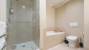 Un baño moderno con ducha envuelta en vidrio, inodoro blanco y un pequeño cubo de basura.