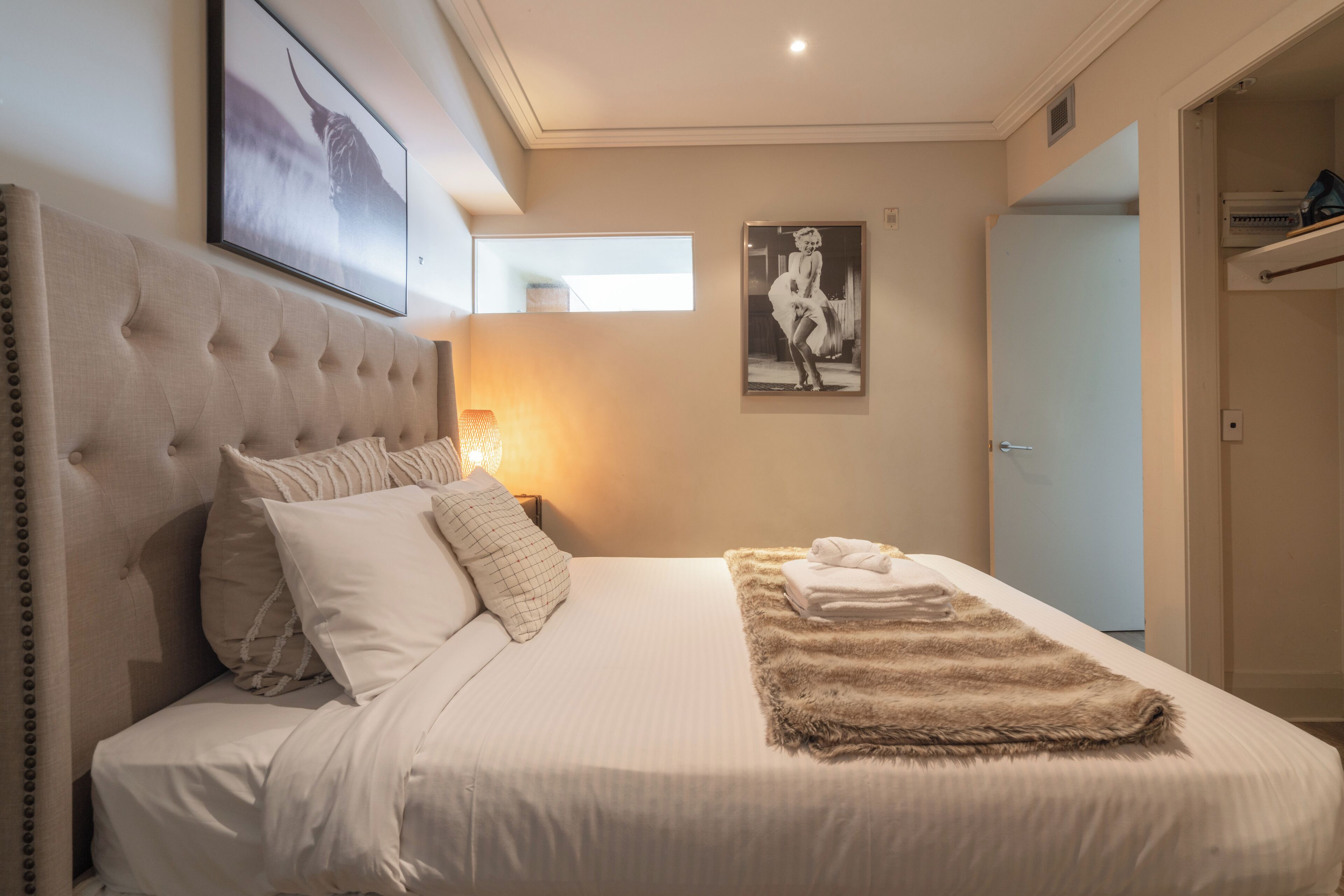 A bedroom with a tufted headboard, a large bed with white linens, a fluffy throw blanket, and a framed picture on the wall.