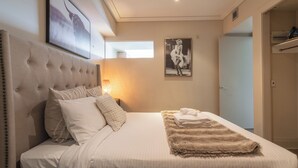 Un dormitorio con cabecera capitonada, cama grande con ropa de cama blanca, manta suave y un cuadro en la pared.