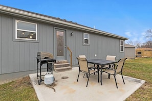 A residential building with a patio area featuring a table and chairs, a grill, and a gas canister. - Stylish MidModern 1 Bed Apartment - Lower Level/Pr (Grandview)