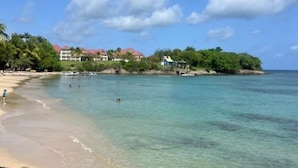 A beach with clear turquoise water, a sandy shore, and buildings with red roofs in the background. - Building Martinique (Sainte-Luce)