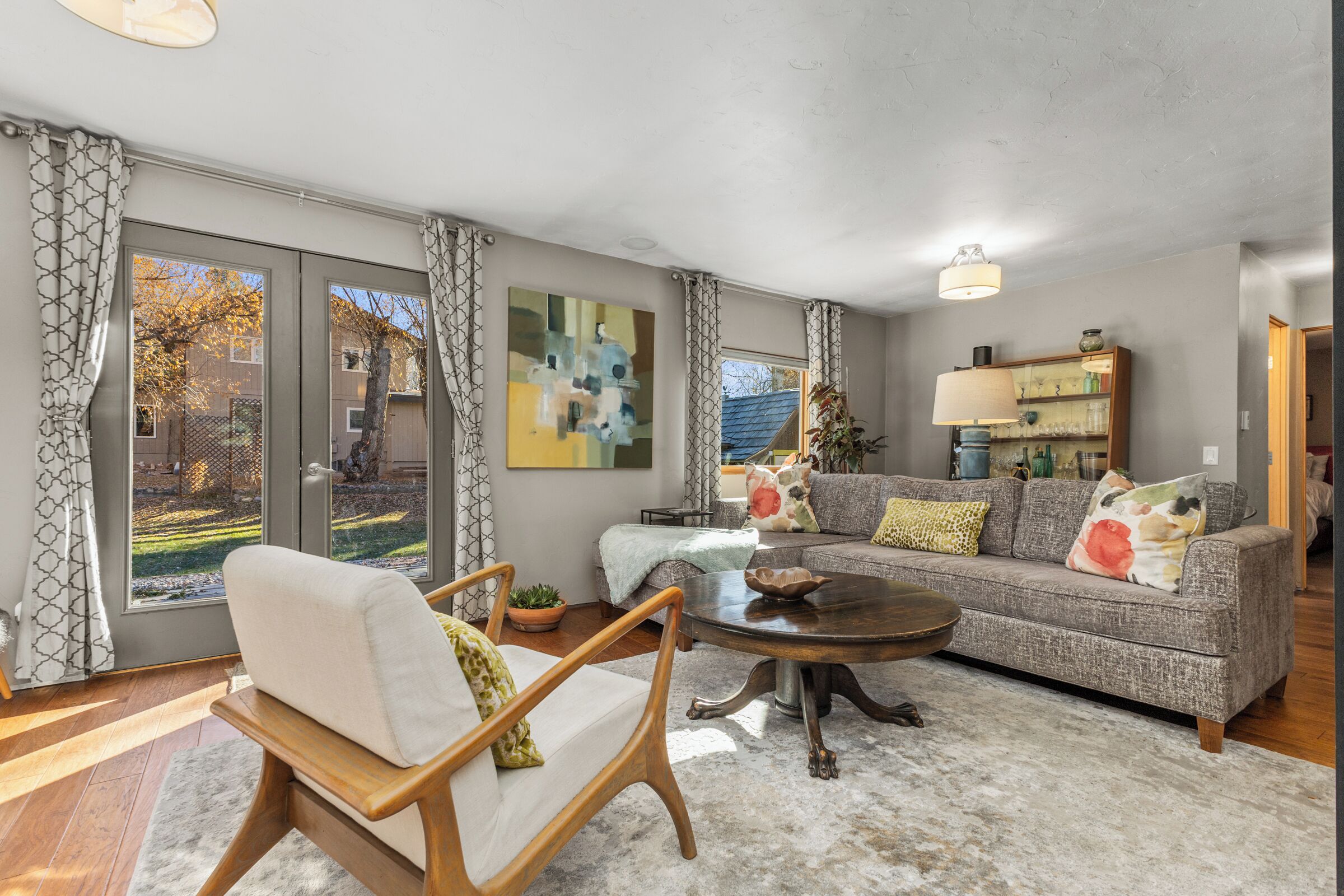 A living room with a sofa, armchair, coffee table, and a large window with curtains.