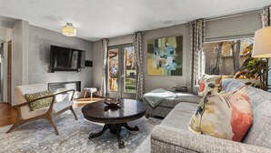A modern living room with a fireplace, a flat-screen TV mounted on the wall, a round coffee table, and a sofa with patterned cushions. - Pet Friendly|Steps from Town|Private yard (Steamboat Springs)