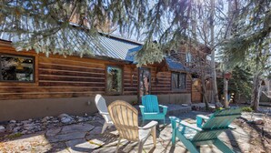 A wooden cabin with a stone patio, two Adirondack chairs, and a small table. - Pet Friendly|Steps from Town|Private yard (Steamboat Springs)