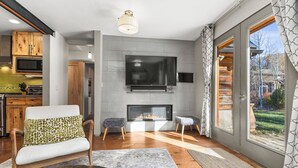 A modern living room with a fireplace, a flat-screen TV, wooden cabinets, and a large window. - Pet Friendly|Steps from Town|Private yard (Steamboat Springs)