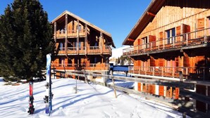 Eine Holzhütte mit Balkonen, eine Skipiste und verschneiter Boden.