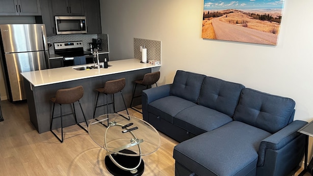 Ett modernt kök med en inbyggd köksö, barstolar och en stor blå soffa.