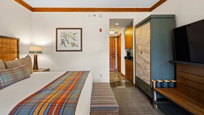 Une chambre d’hôtel comprenant un lit, un banc, une télévision, un tableau et un coin cuisine.
