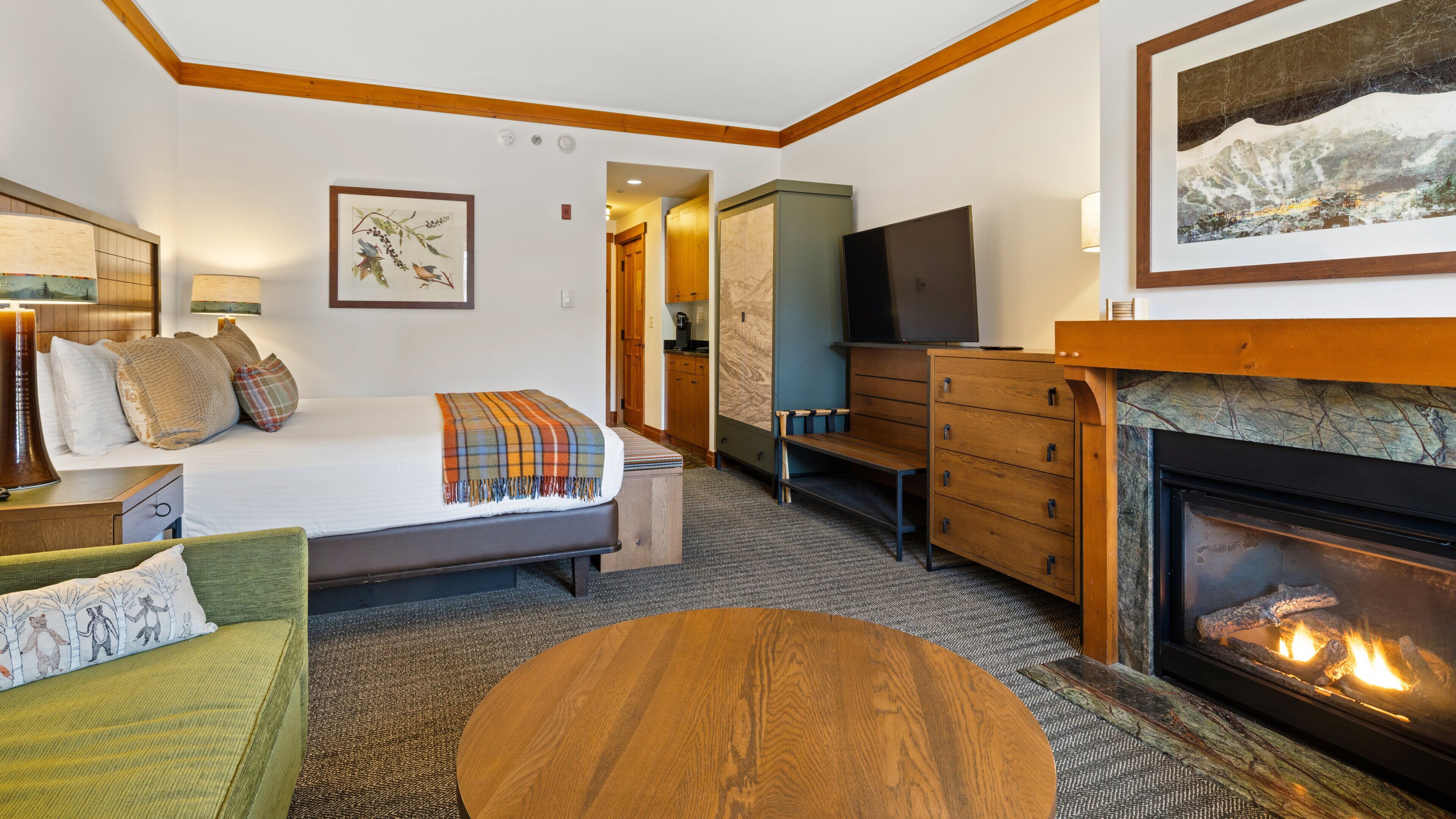 Una habitación de hotel con cama, sofá, cómoda de madera, televisor y chimenea.