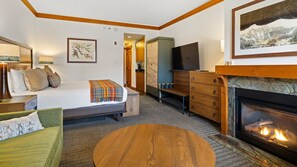 Une chambre d’hôtel comprenant un lit, un canapé, une commode en bois, une télévision et une cheminée.