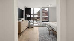 Ein modernes Schlafzimmer mit großem Fenster, einem Bett, einem Fernseher und einer Kommode.