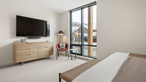 Ein modernes Schlafzimmer mit großem Fenster, einem Flachbildfernseher, einer Holzkommode, einem Stuhl und einem Bett.