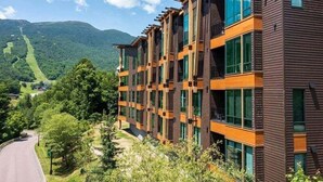 Ein mehrstöckiges Gebäude mit modernem architektonischen Design, das große Fenster und eine Kombination aus dunklen und hellen Holzwandverkleidungen zeigt.