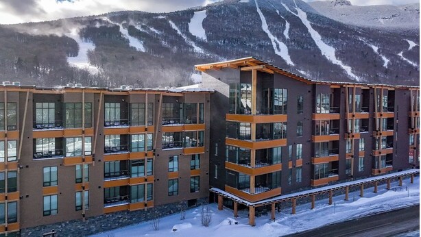 Ein modernes, mehrstöckiges Hotel mit großen Fenstern und Balkonen vor einer verschneiten Berglandschaft.