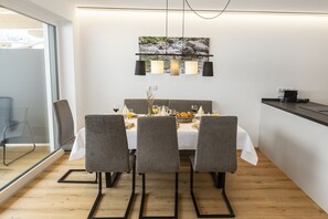 A modern dining area with a white table, grey upholstered chairs, and a wooden floor. - Alpine Apartment With Dream View & Garden Feeling (Wildschönau)