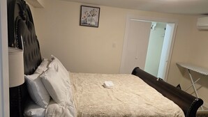 Ein Schlafzimmer mit einem Bett, einem Nachttisch, einer Lampe, einem Wandbild, einer Tür und einem kleinen Tisch mit Stuhl.
