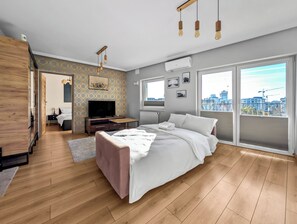 Une chambre moderne avec un grand lit, une télévision et une vue sur la ville, visible à travers la porte-fenêtre coulissante.