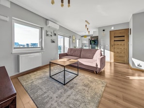 A modern living room with a sofa, a coffee table, and a view of the city through large windows. - Kurkowa Cozy Apartment (Wrocław)