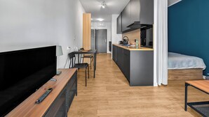 Et moderne hotelværelse med fladskærms-tv, træmøbler, tekøkken og en seng mod en blå væg.